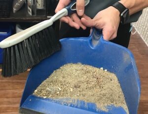 Rug Specialist shows off dust pan filled with soil removed from an area rug.
